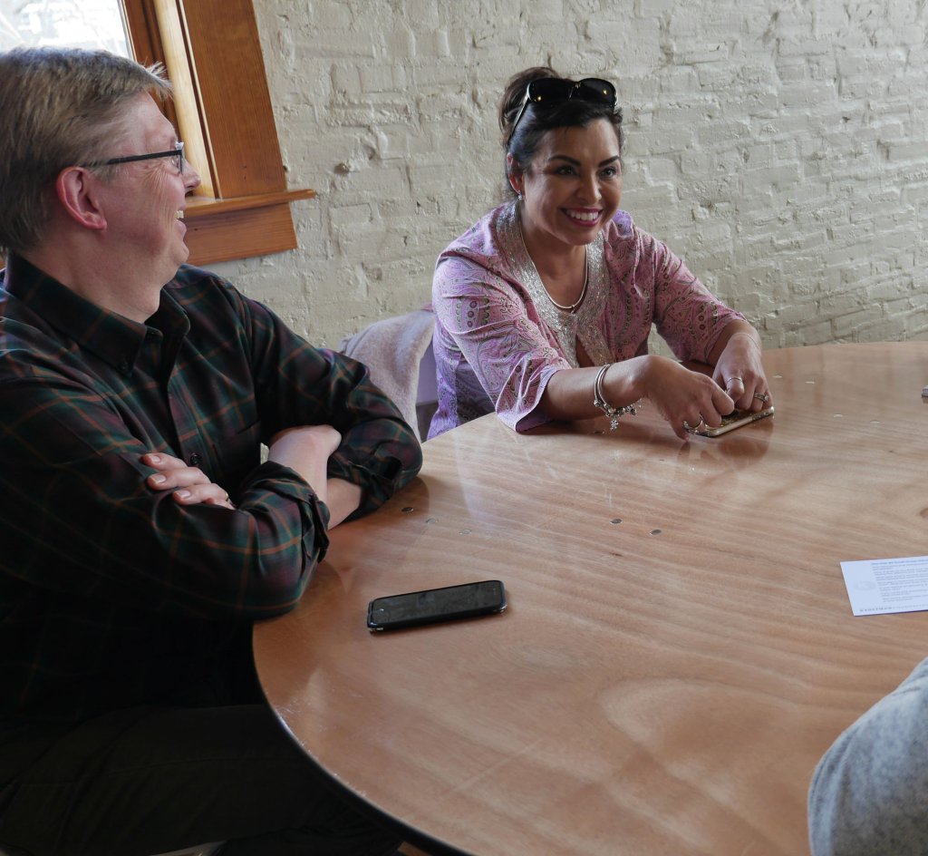 Two people sit at a rounded table in a group conversation with others not pictured.